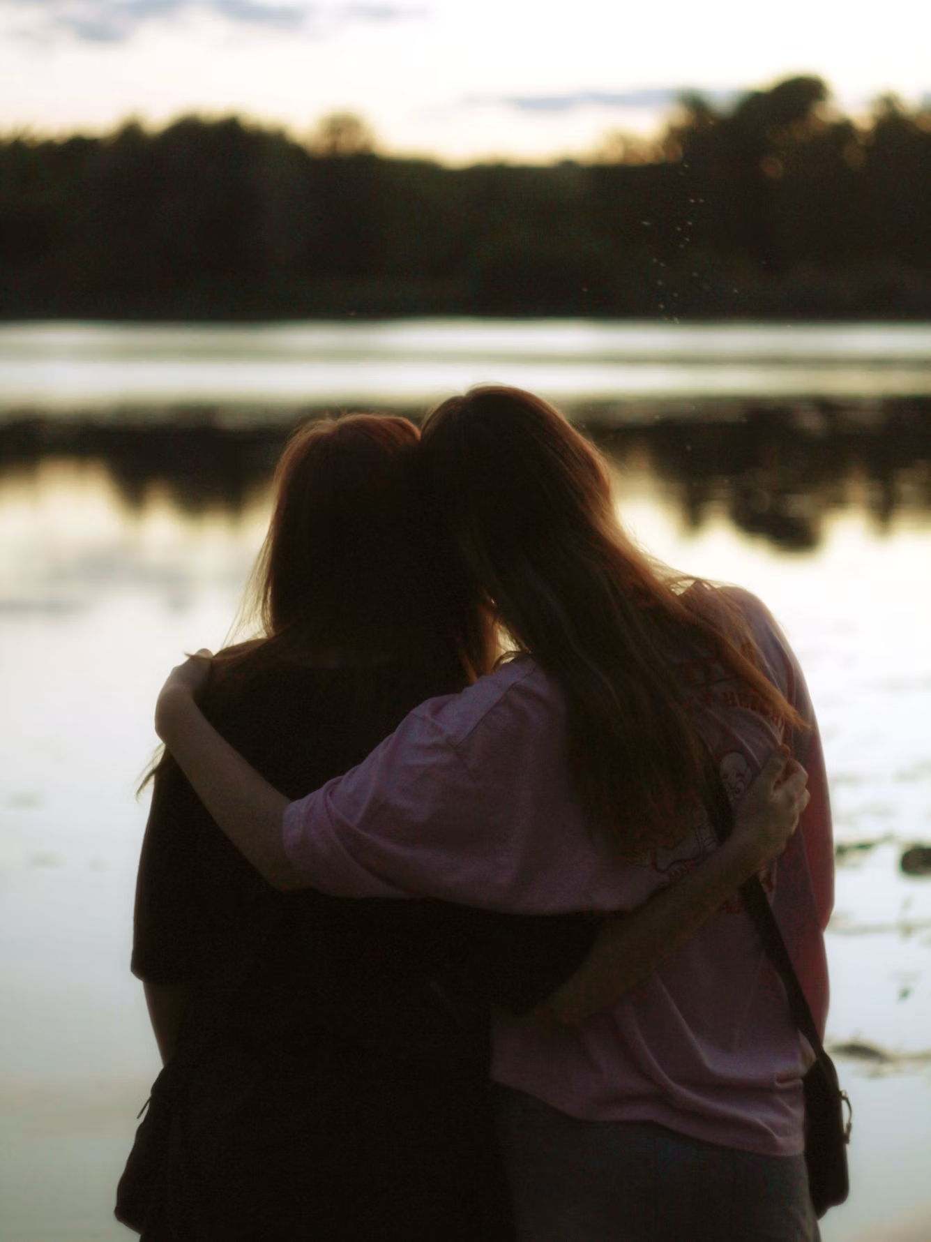Dos personas abrazadas frente a un lago al atardecer