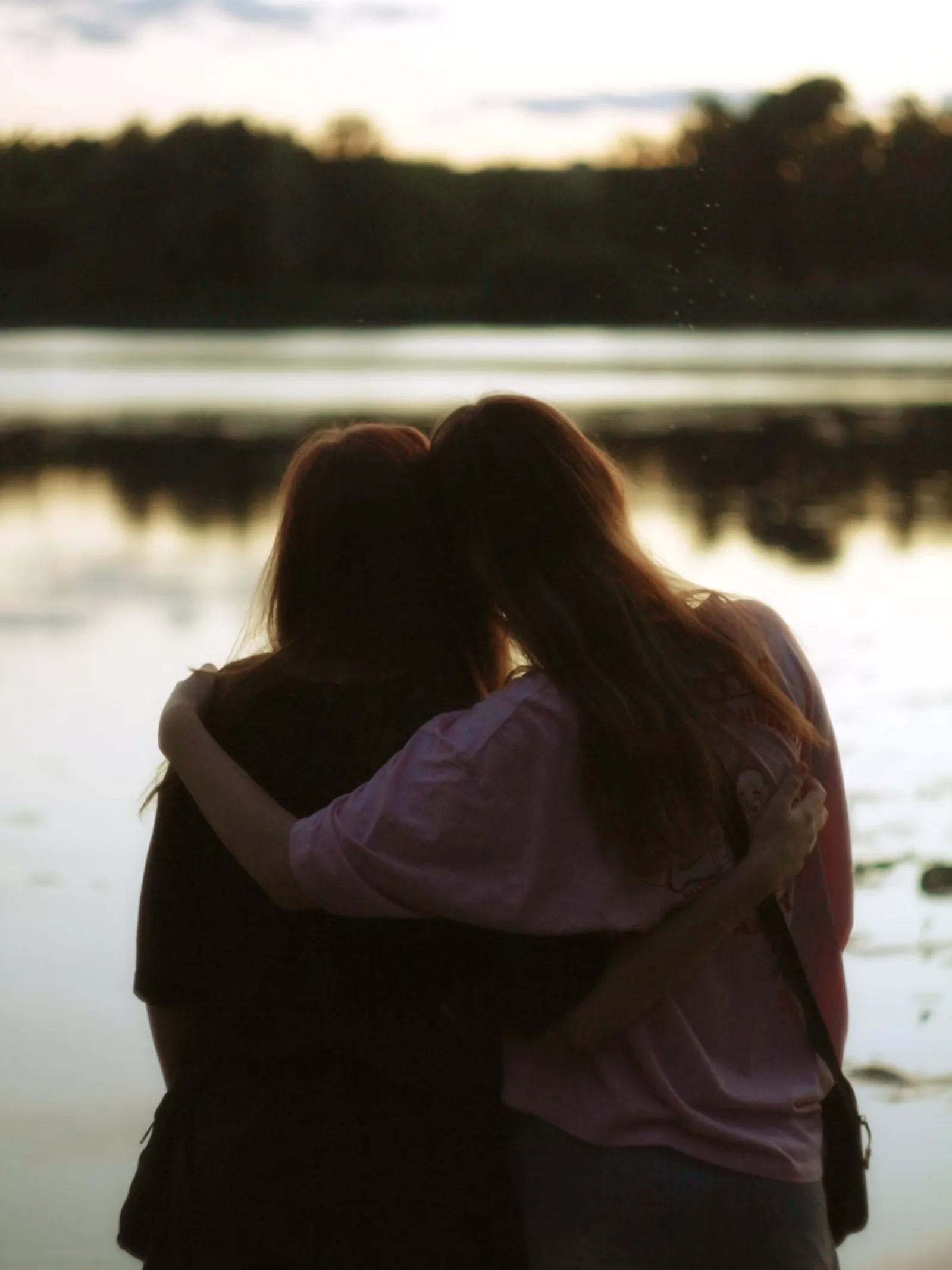 Dos personas abrazadas frente a un lago al atardecer